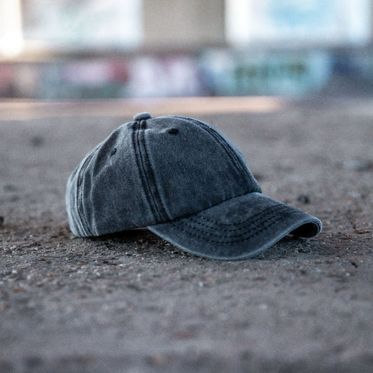 Voorkant van een grijs gewassen denim kinderpet op een ruwe betonnen ondergrond met vage graffiti op de achtergrond.