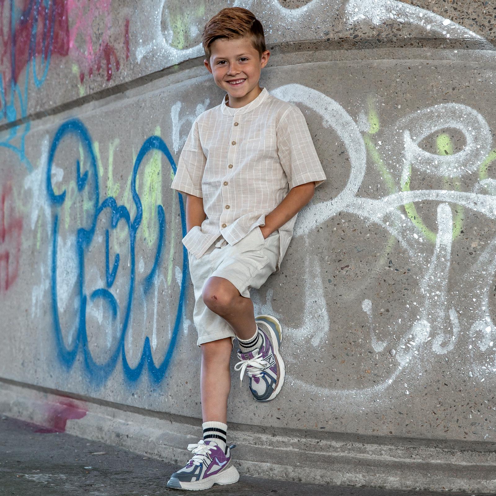 Jongen leunend tegen muur met Twistz Purple sneakers aan, comfortabele en stoere kinderschoenen van Lilpataz